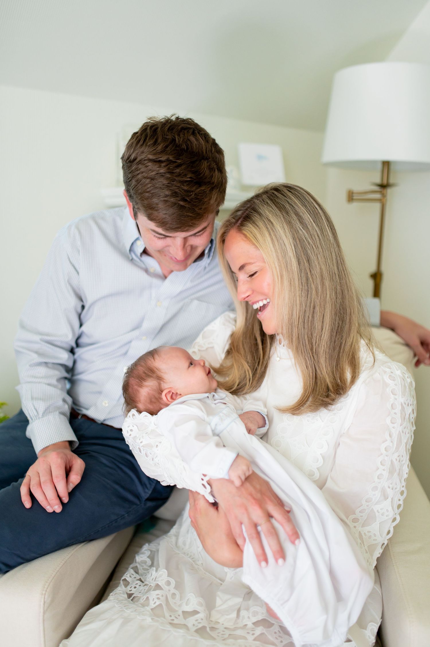 Happy parents smiling at their newborn baby while sitting together on a couch in a bright, cozy room.