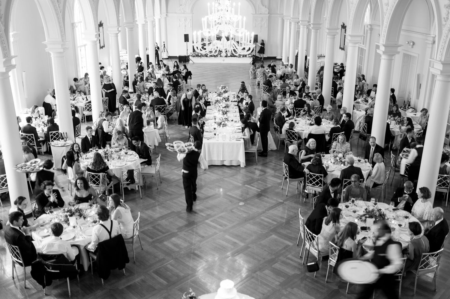 Panoramic view of a luxurious wedding reception venue with white columns and crystal chandeliers.