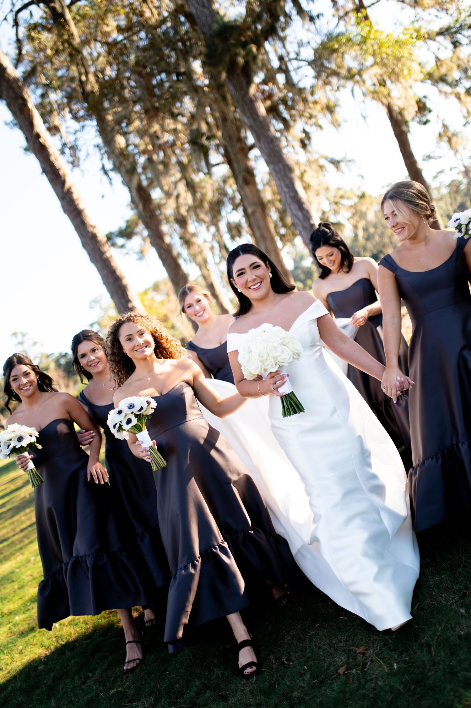 Bridesmaids in navy dresses pose playfully with bride on grassy lawn.