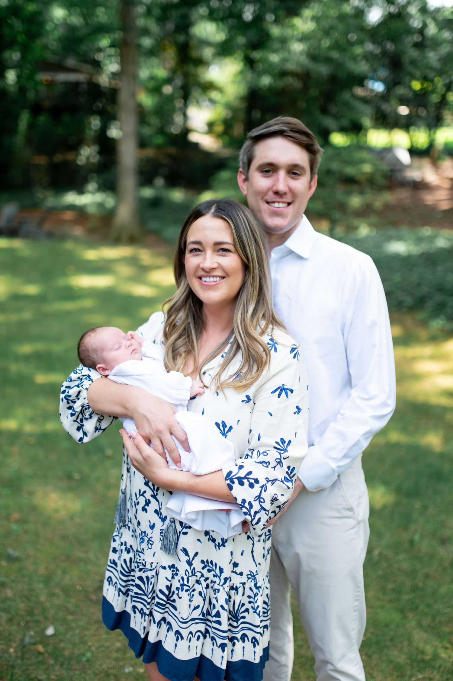 Outdoor family portraits in a sunlit garden wearing coordinating white and blue floral outfits.