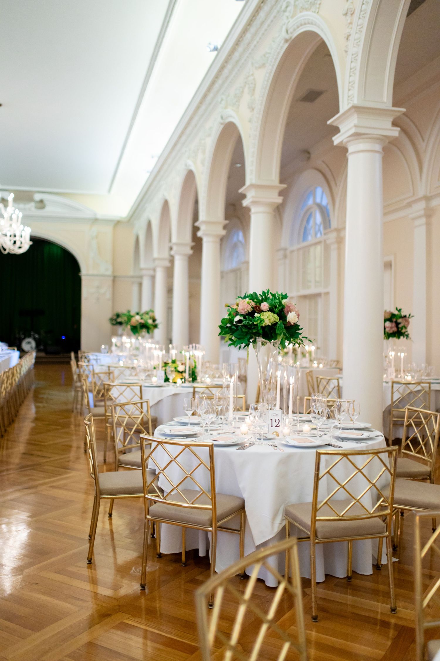 An elegant wedding reception venue with white tables and gold chairs under arched columns.