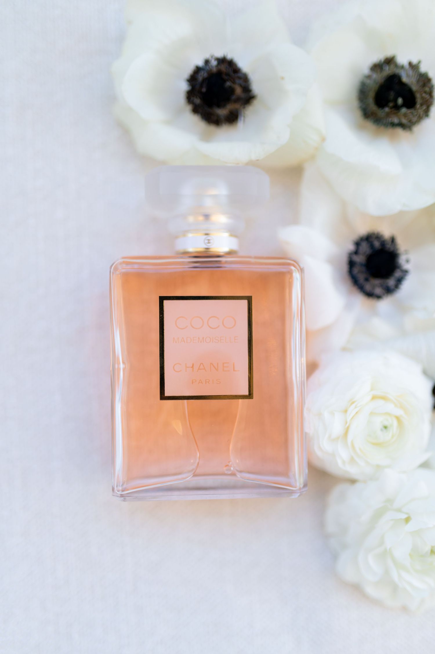 Pink perfume bottle surrounded by delicate white anemone flowers on light background.