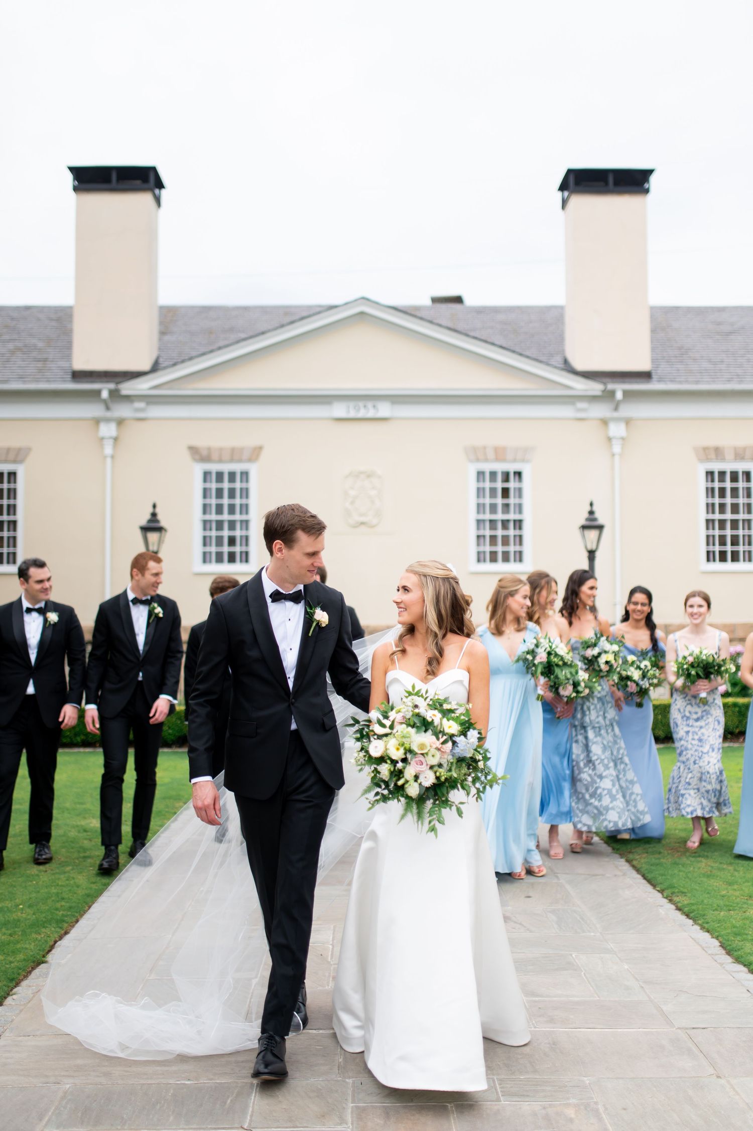 Wedding party poses outside a classic colonial-style building with light blue bridesmaid dresses.