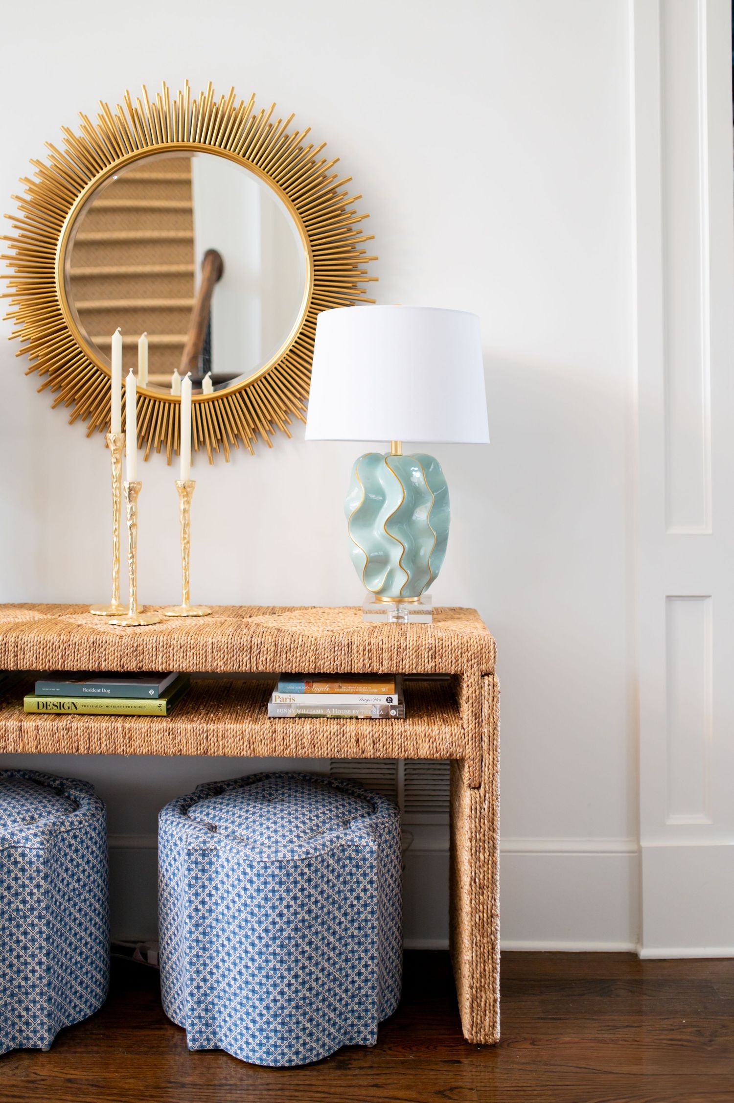 Three identical grasscloth console tables with sunburst mirrors and blue ottomans create a stylish entryway display.