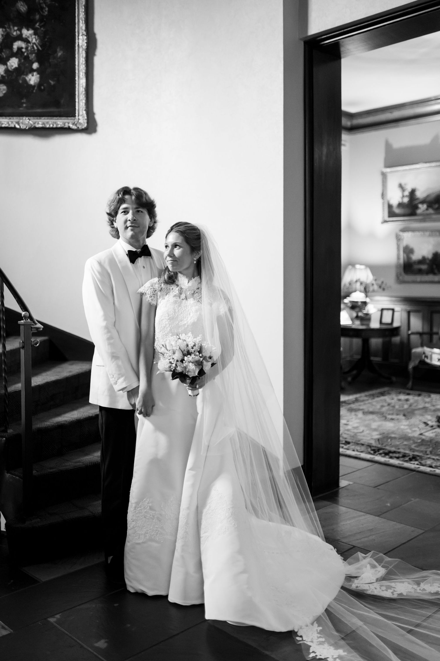 Elegant black and white wedding portrait showing a bride in a flowing white gown and veil against an interior backdrop.