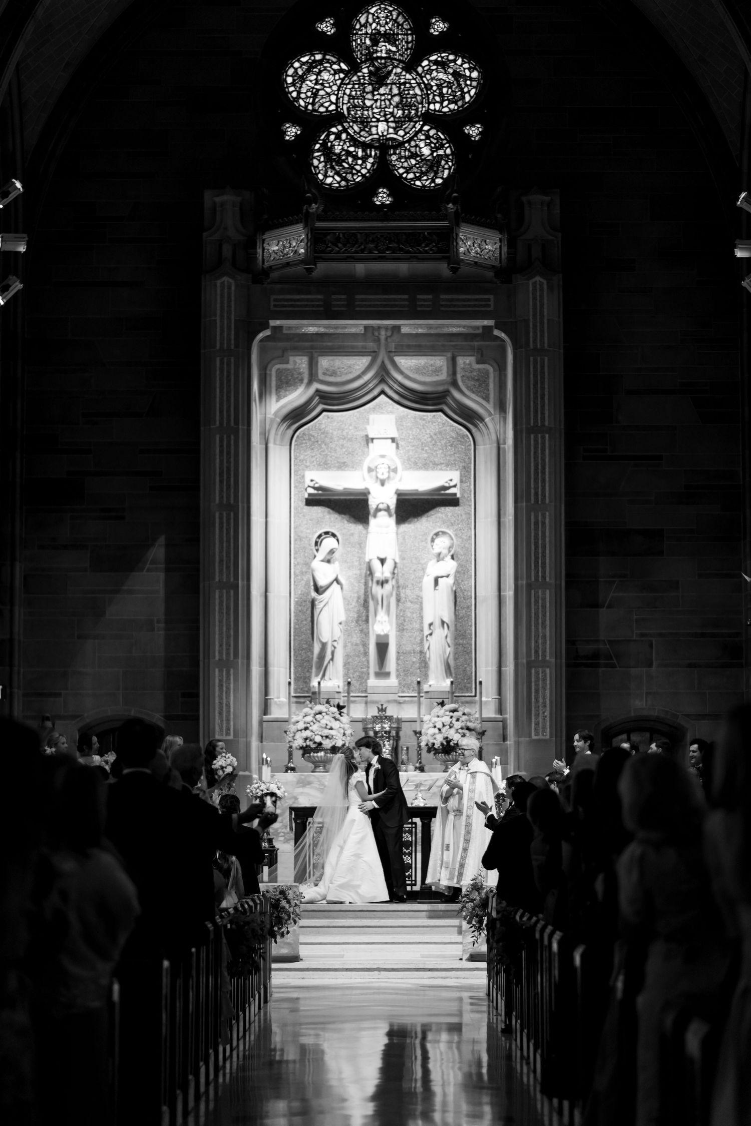Black and white photo of a wedding ceremony in a cathedral with dramatic backlighting.