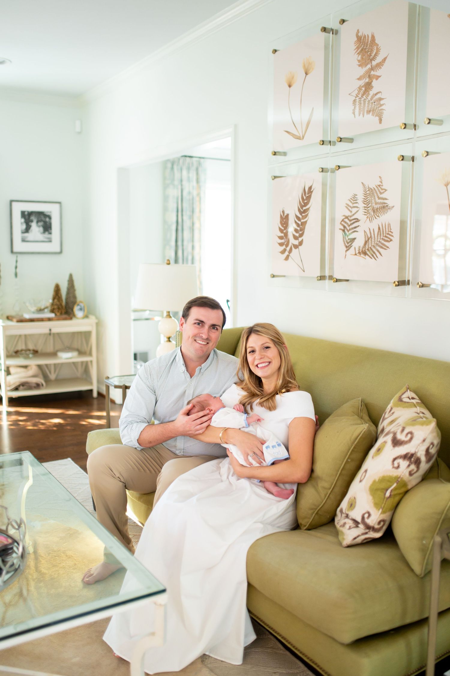 A couple sits together on an olive green couch in a bright room with botanical artwork on the walls.