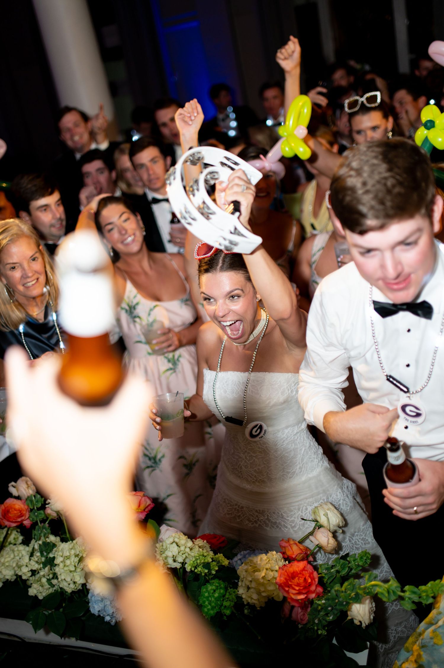 Bride dances energetically with tambourine at lively wedding reception surrounded by guests.