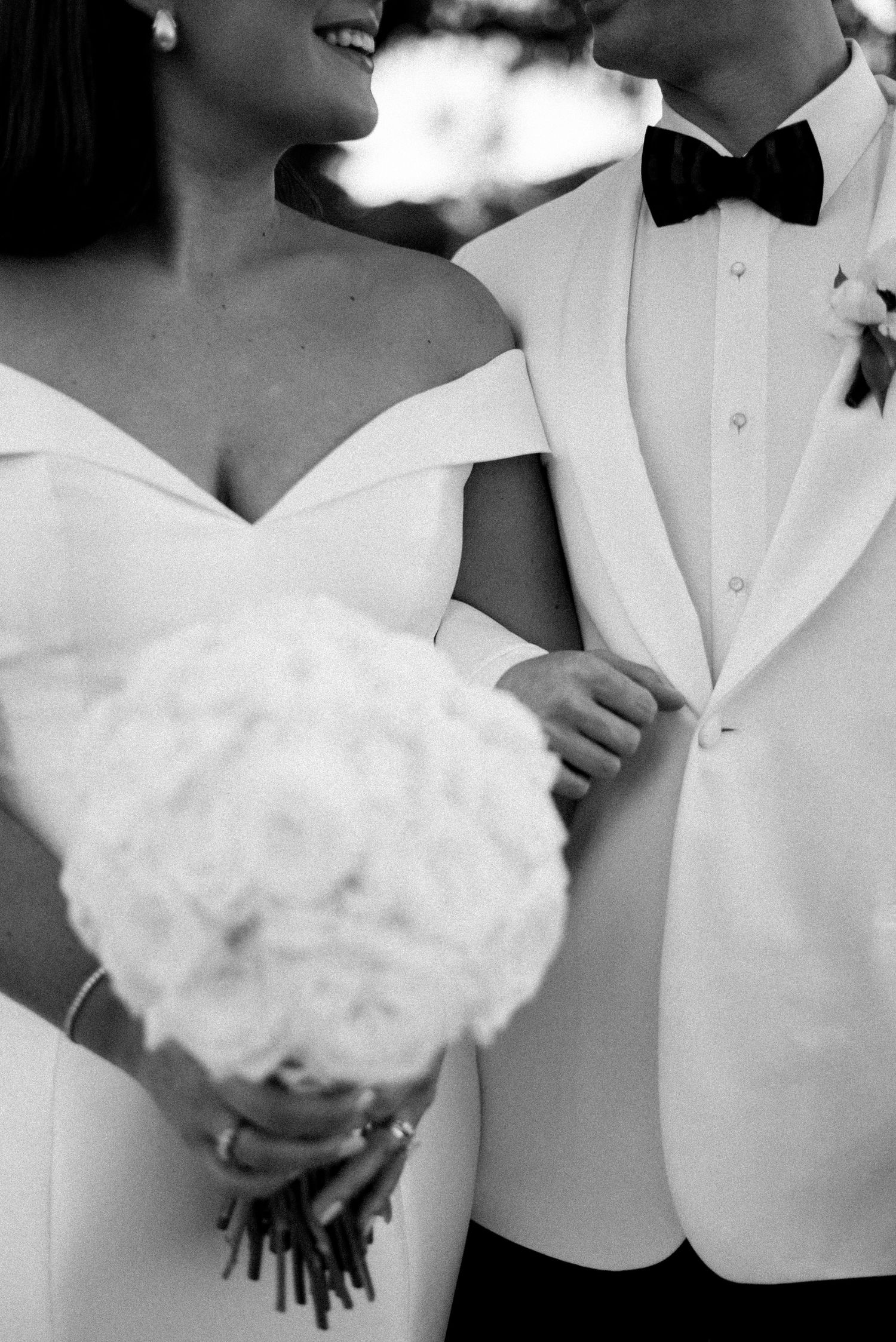 Black and white close-up of couple with white bouquet and formal attire.