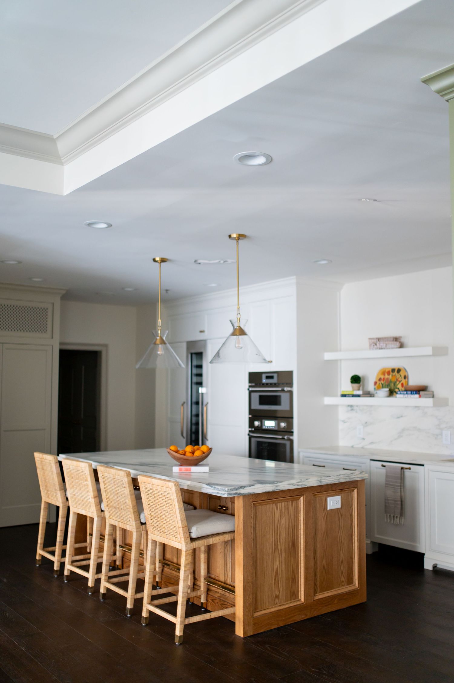Modern kitchen with wood and marble island, pendant lights, and built-in appliances featuring light wood bar stools.