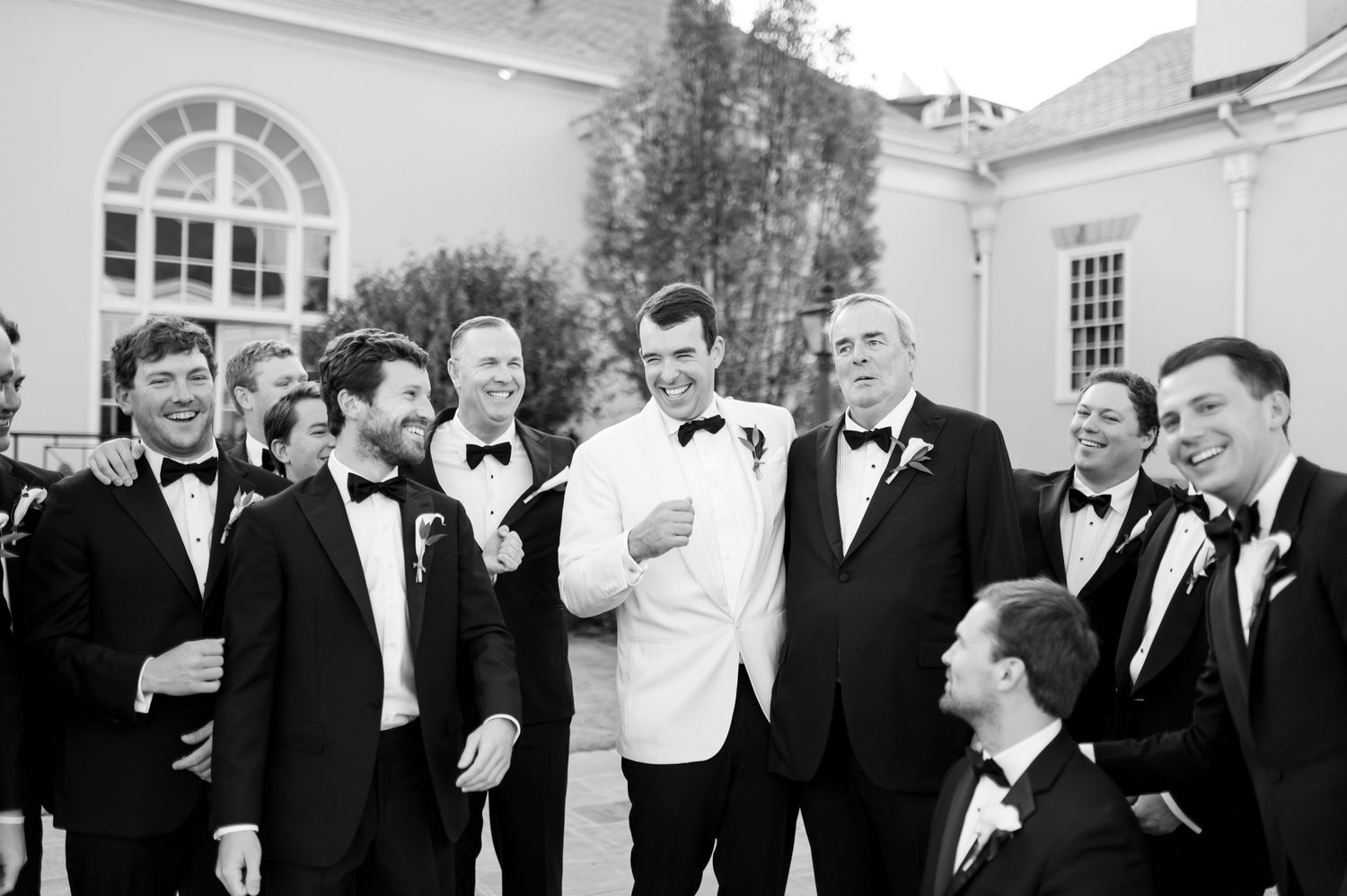 Groomsmen in black tuxedos share a candid laughing moment together during wedding photos.