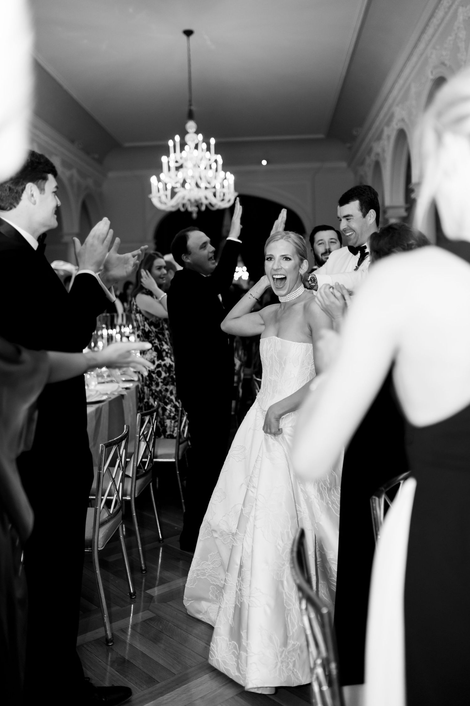 Wedding celebration in an elegant ballroom with guests dancing under crystal chandeliers.
