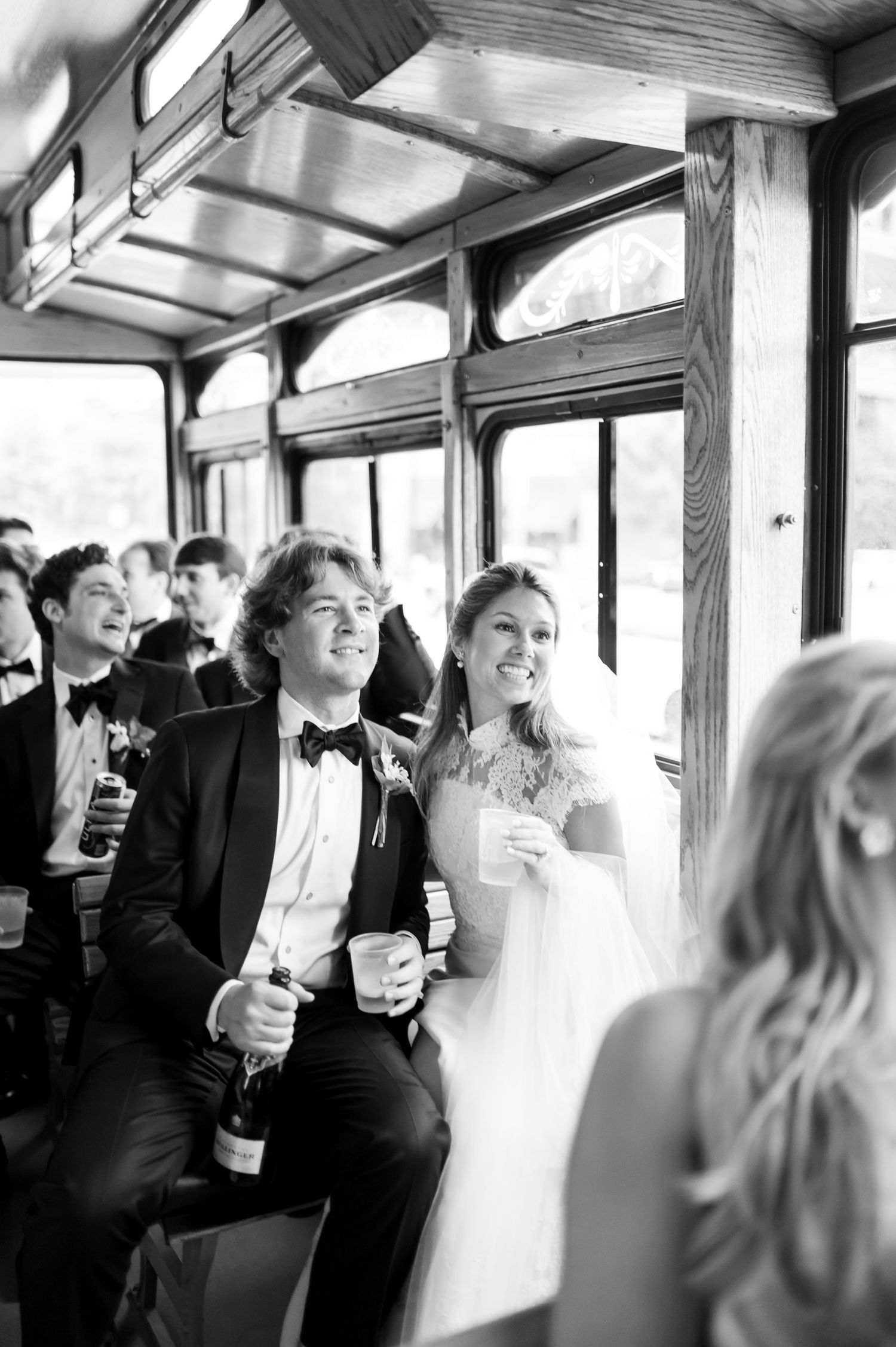 Wedding party celebrates with champagne while riding in a vintage trolley car.