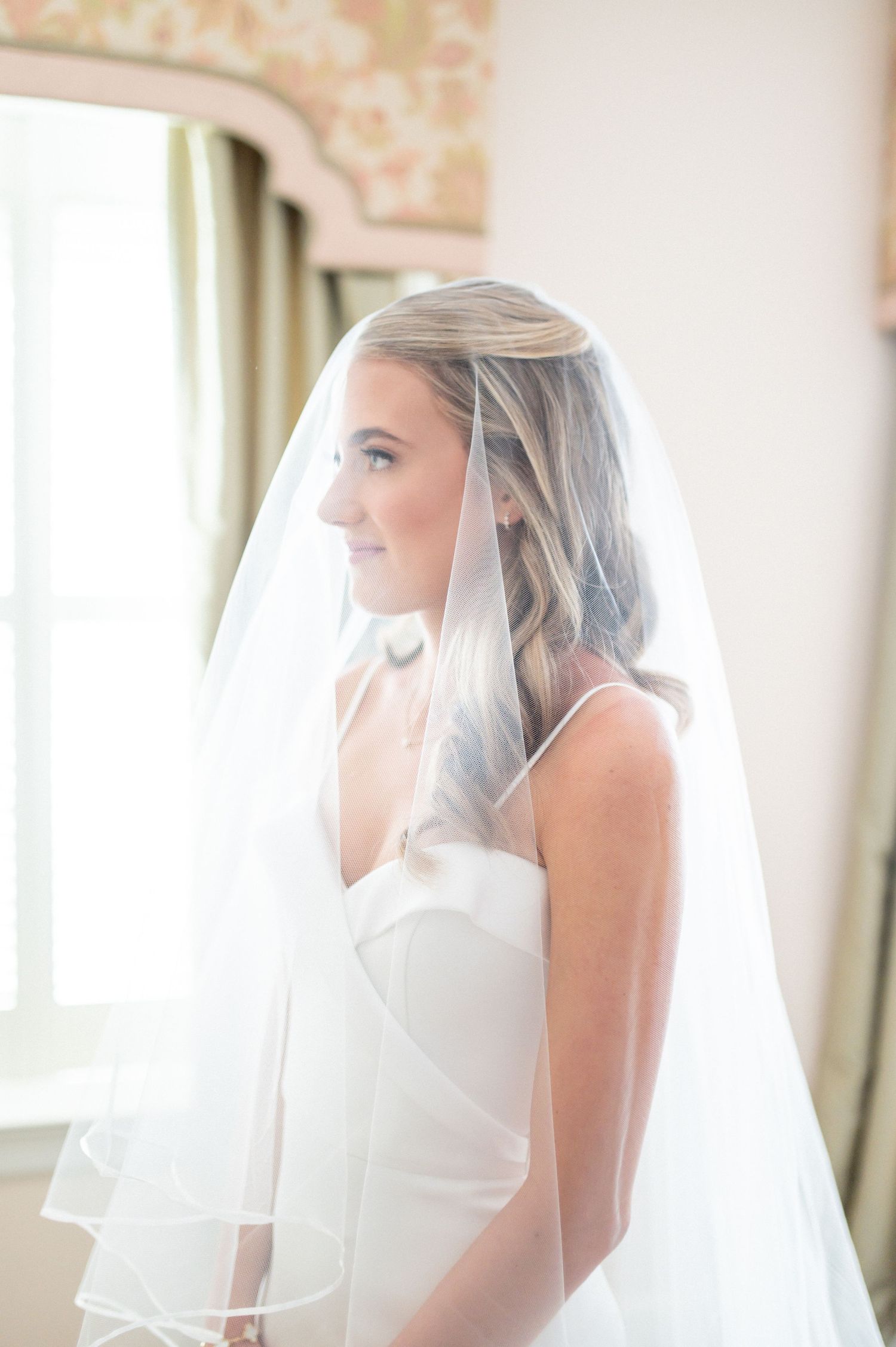 Side profile of bride wearing an elegant white wedding gown and flowing veil.