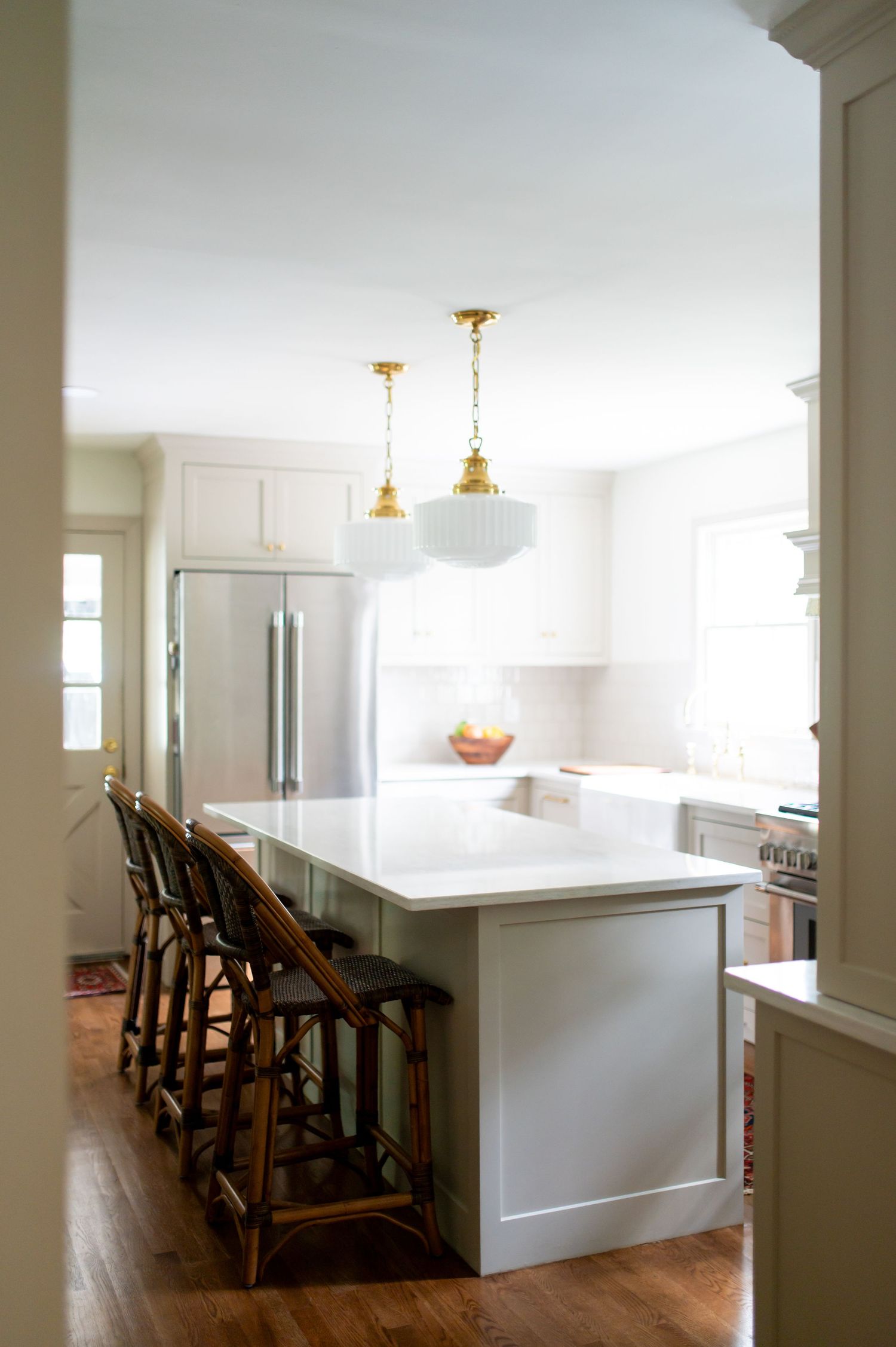 Modern white kitchen with large island, wooden barstools, hardwood floors and vintage glass pendant lights.