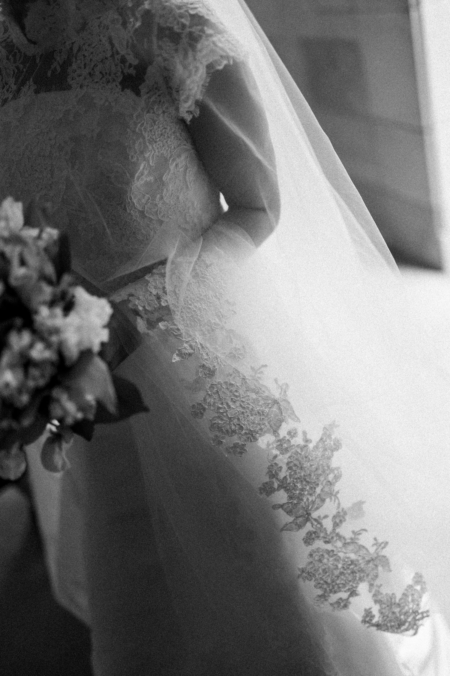 Delicate lace detail on white wedding dress veil shown in black and white photography.