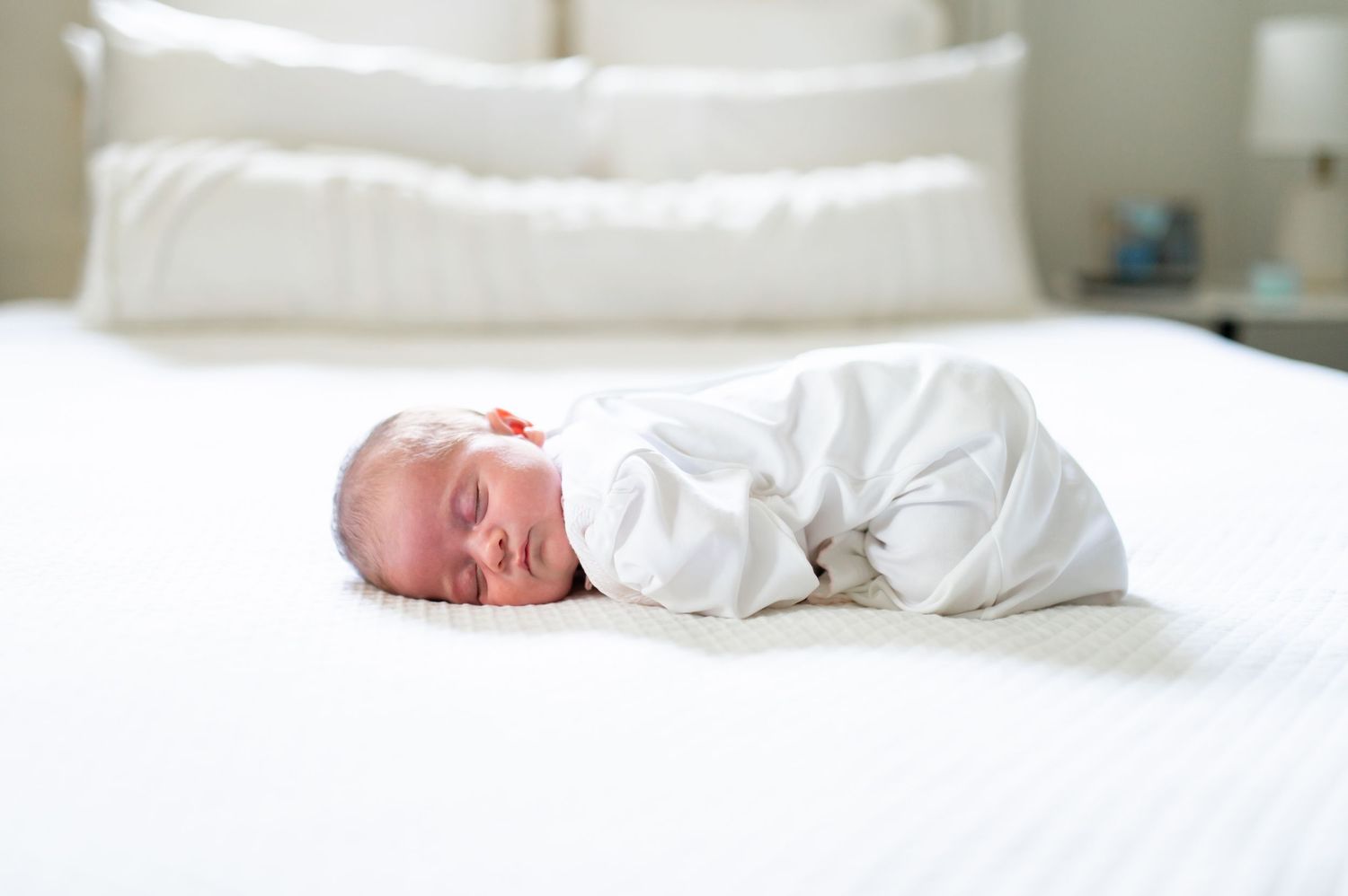 Peaceful newborn sleeping on white bedding in natural light.