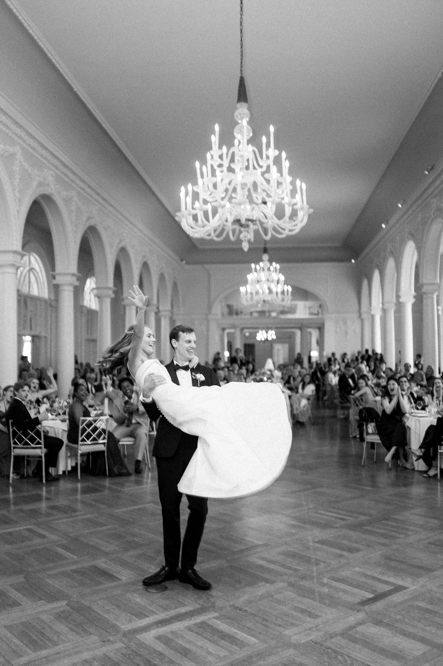 Wedding couple performs romantic dance moves in grand ballroom surrounded by guests.