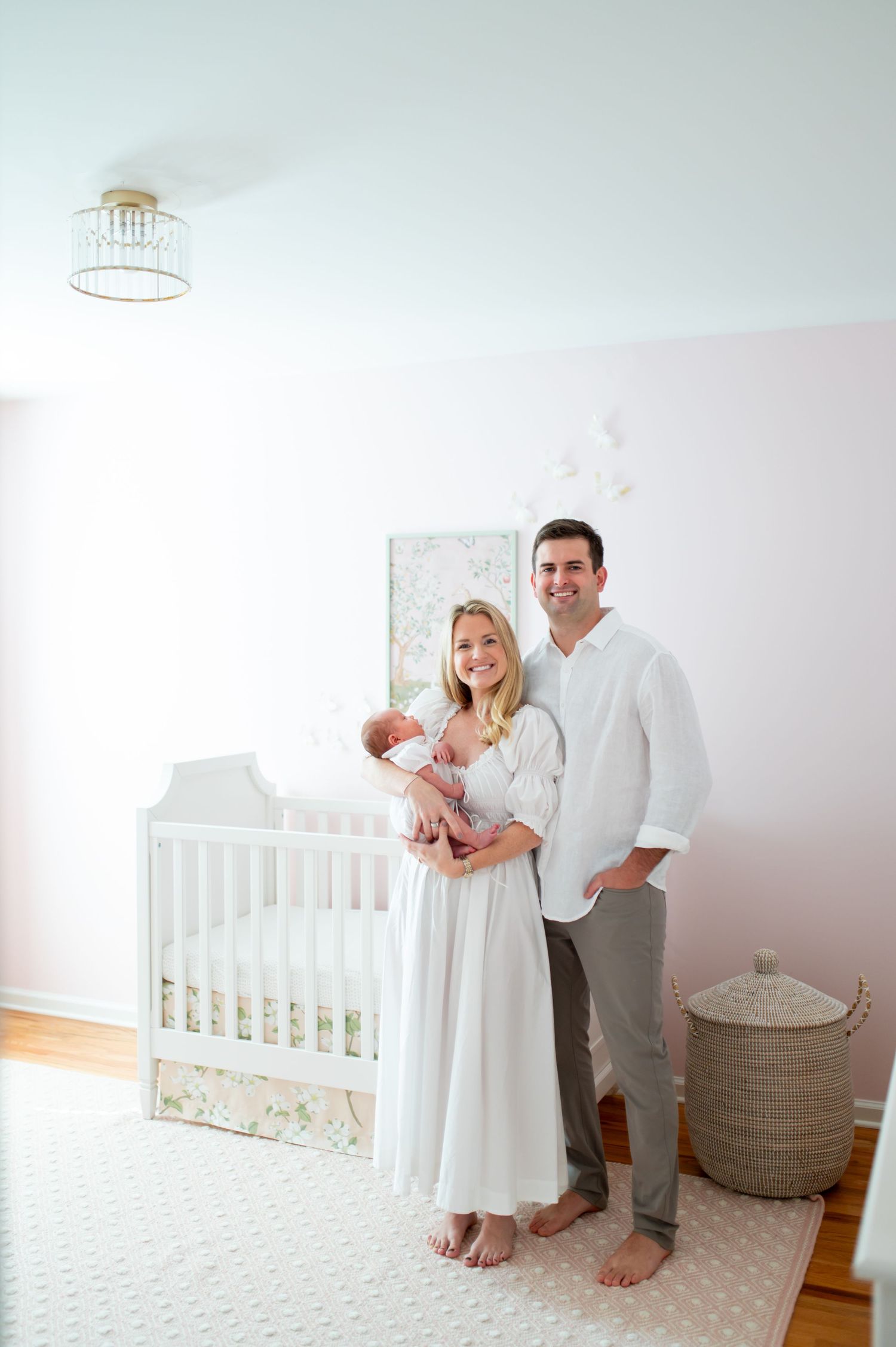 A nursery scene with white decor featuring a crib and family members in light colored clothing.