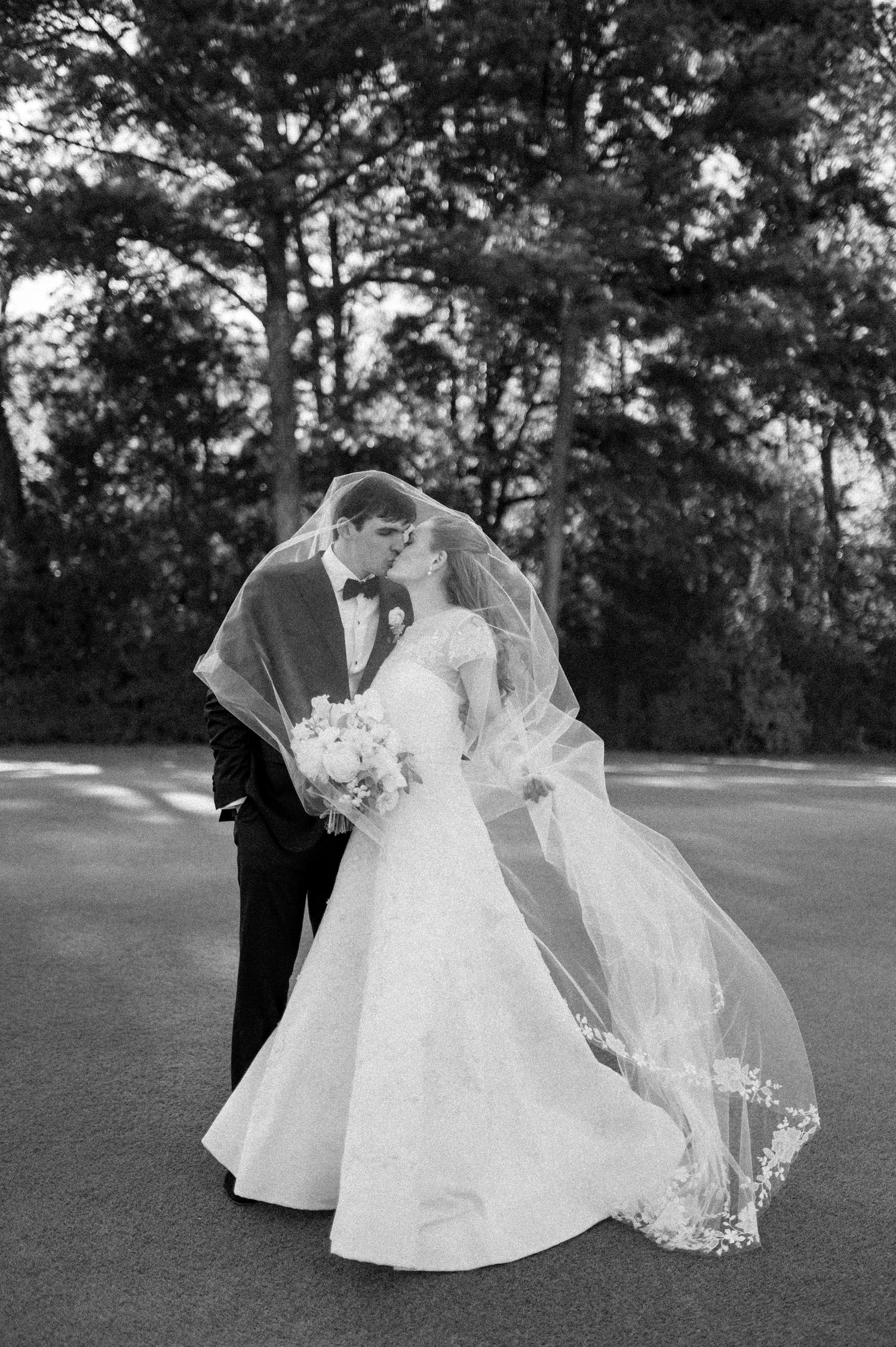 Black and white photo of bride and groom kissing with flowing veil billowing in the wind.