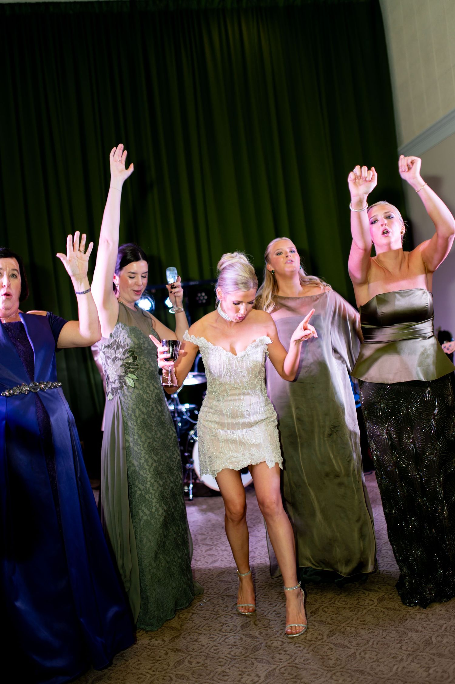 Wedding party members dance and celebrate with raised arms in formal attire.