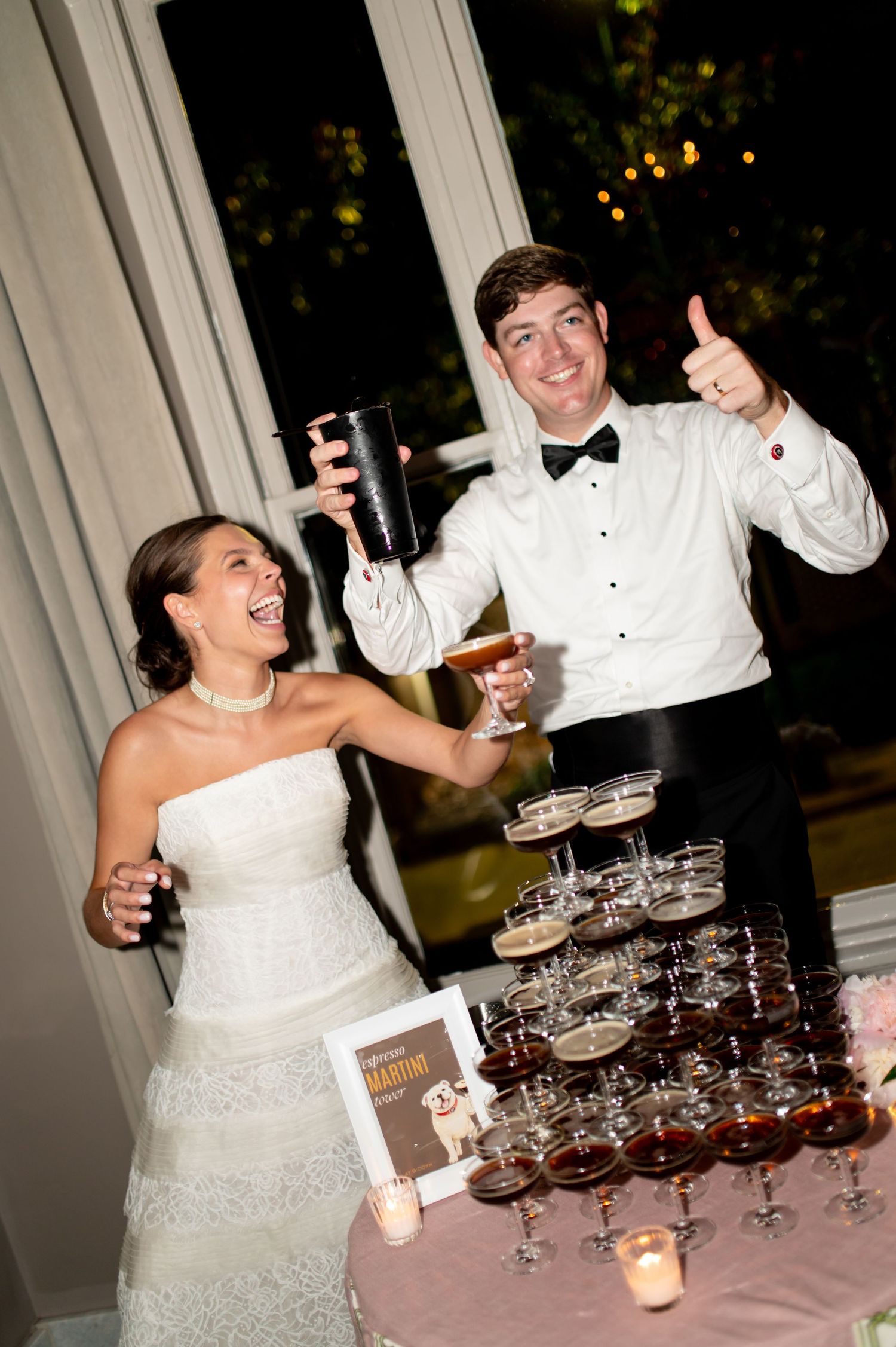 Bride and groom celebrate enthusiastically beside an espresso martini tower at wedding reception.