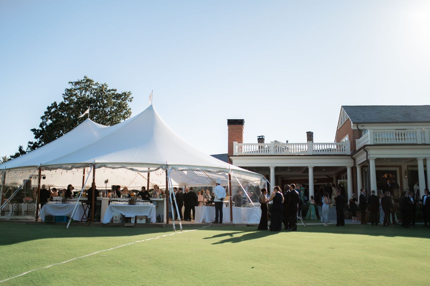 Elegant outdoor wedding reception under white sailcloth tent on golf course at dusk.