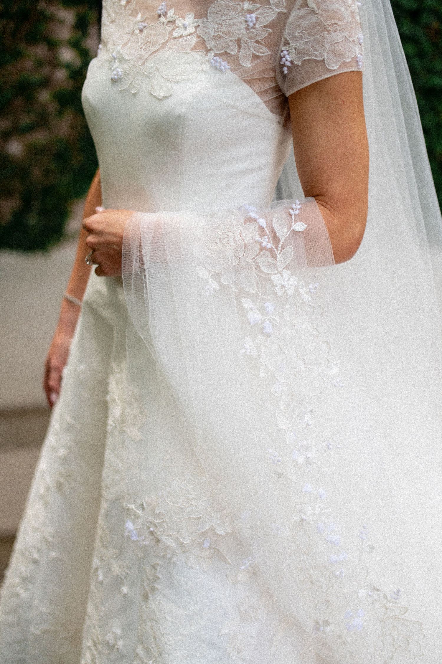 Close-up of bride in elegant lace wedding gown with floral appliques and sheer veil.