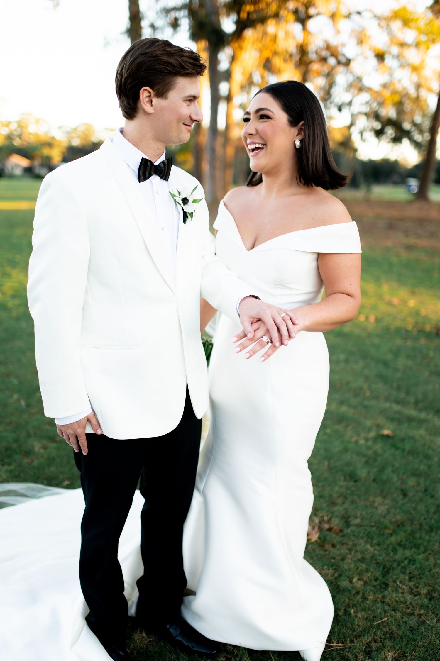 Joyful wedding couple laughs together during outdoor photo session in formal attire.