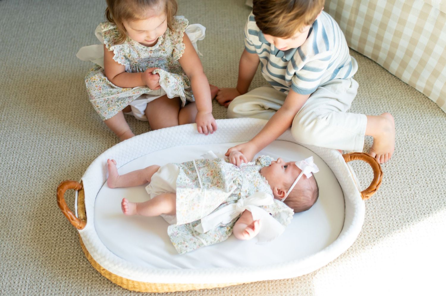Two children sitting on a couch looking down at a baby lying on a white oval tray.