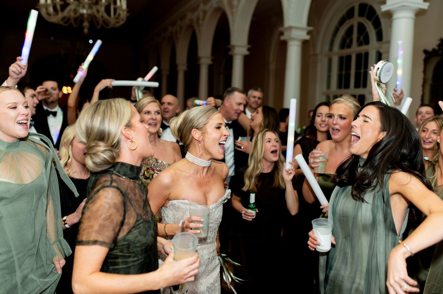 Energetic wedding party dancing and celebrating in a grand ballroom with columns.