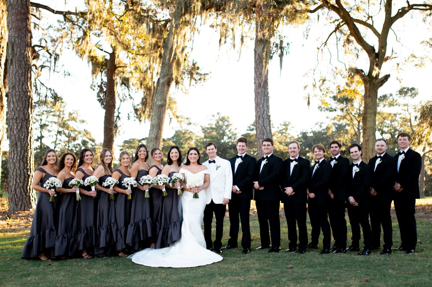 Large wedding party lined up for formal photo with bridesmaids in black and groomsmen in dark suits.