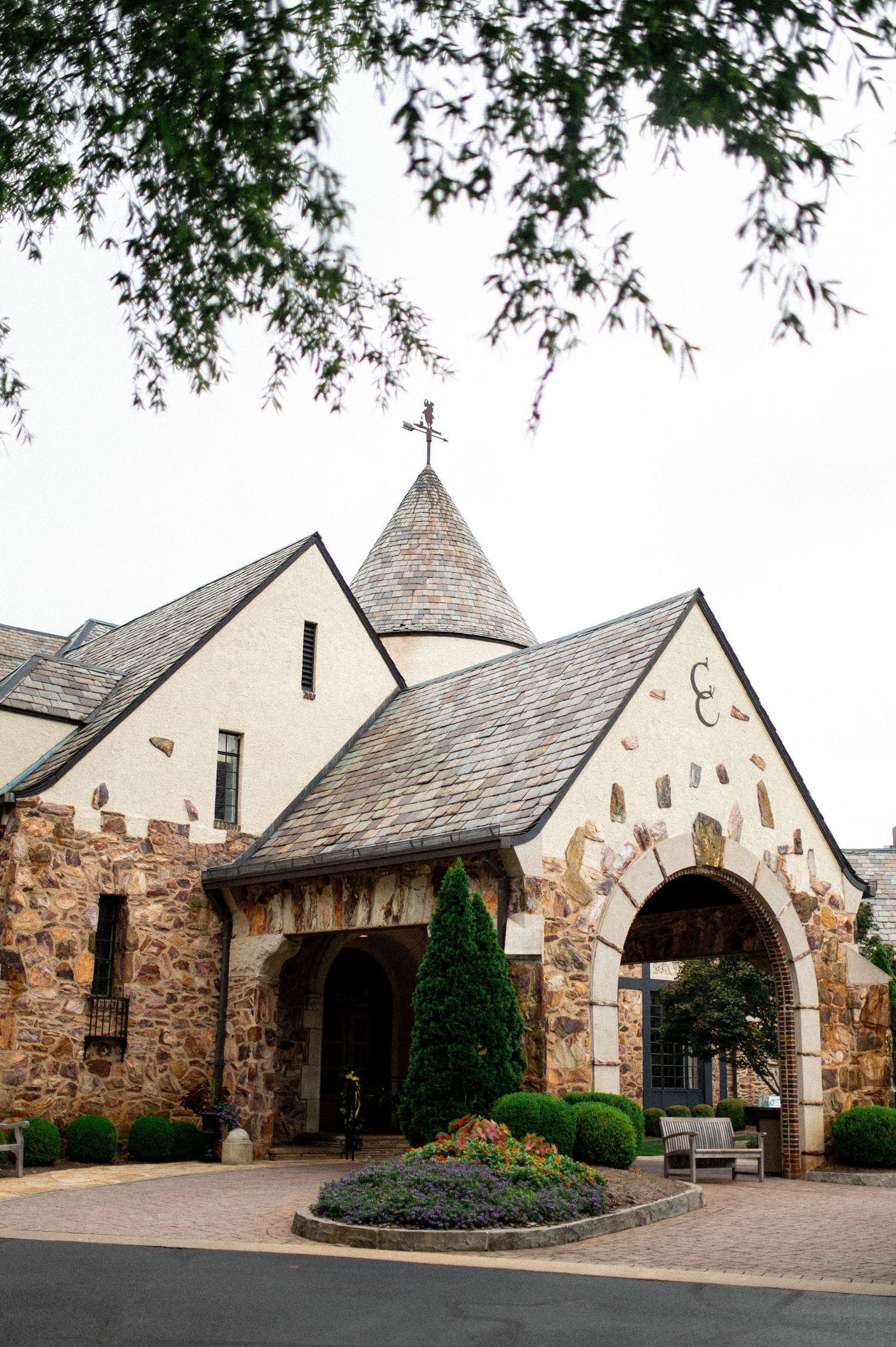 Exterior view of a rustic stone church building with multiple arched entrances and landscaped grounds.