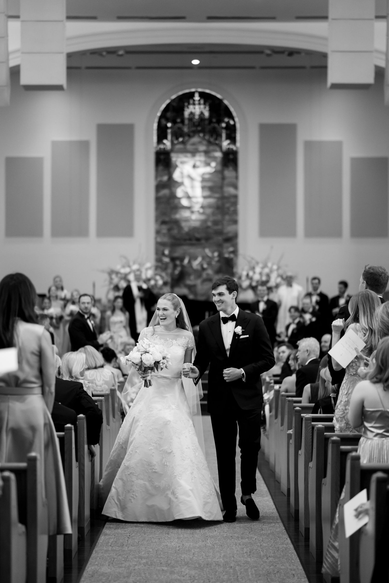 Black and white photo of bride and groom walking down church aisle after wedding ceremony.