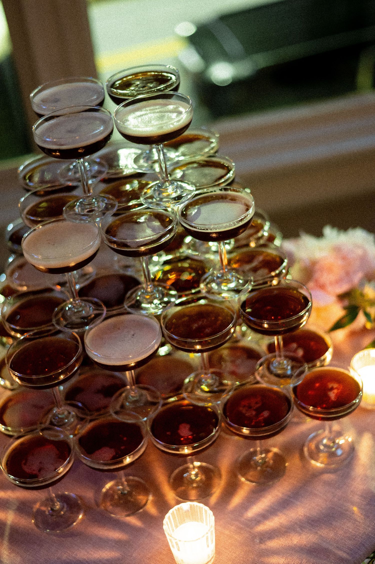 Pyramid tower of espresso martinis in coupe glasses glowing in candlelight at wedding reception.