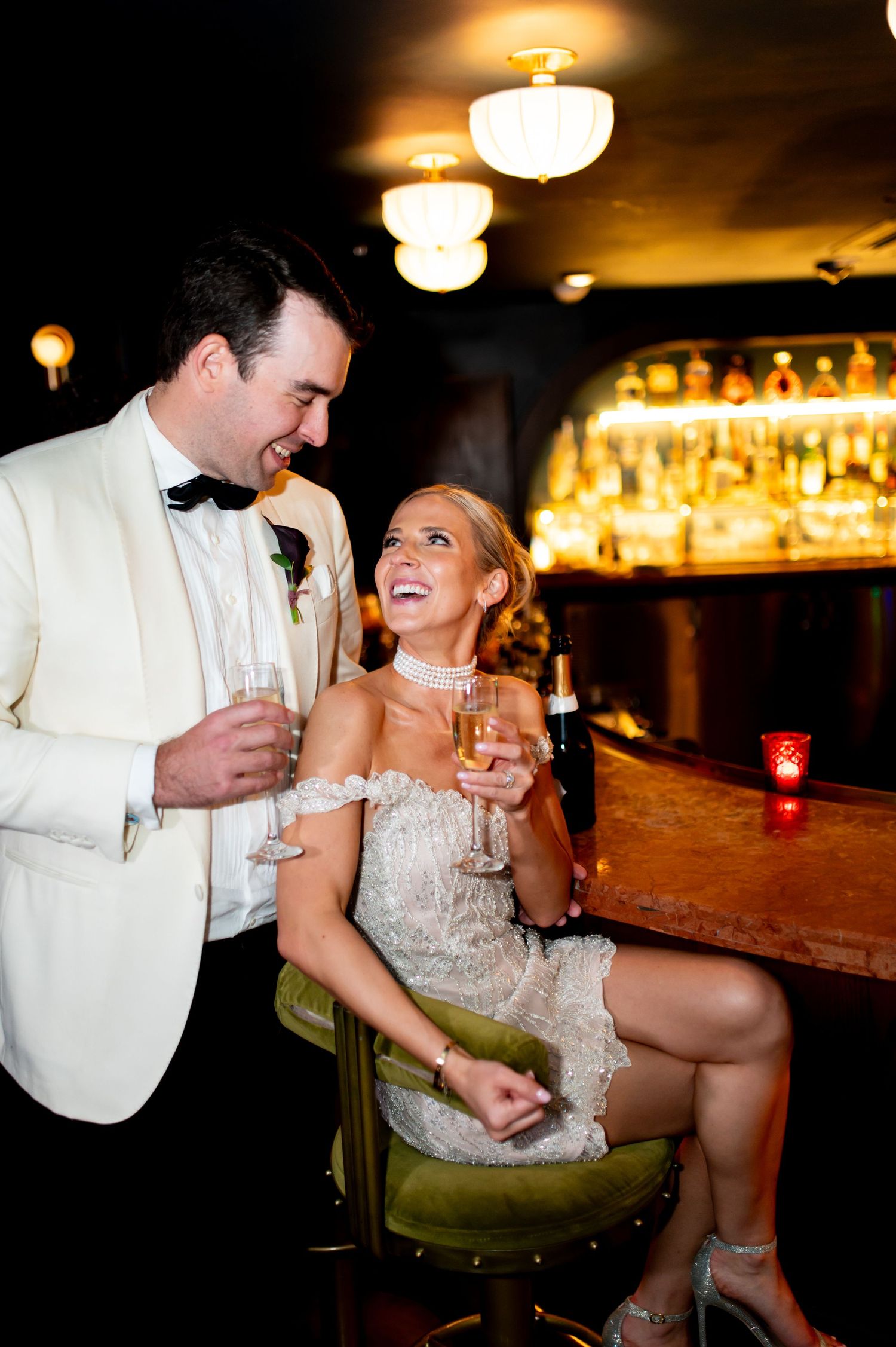 Couple shares champagne and laughter at dimly lit bar during celebration.