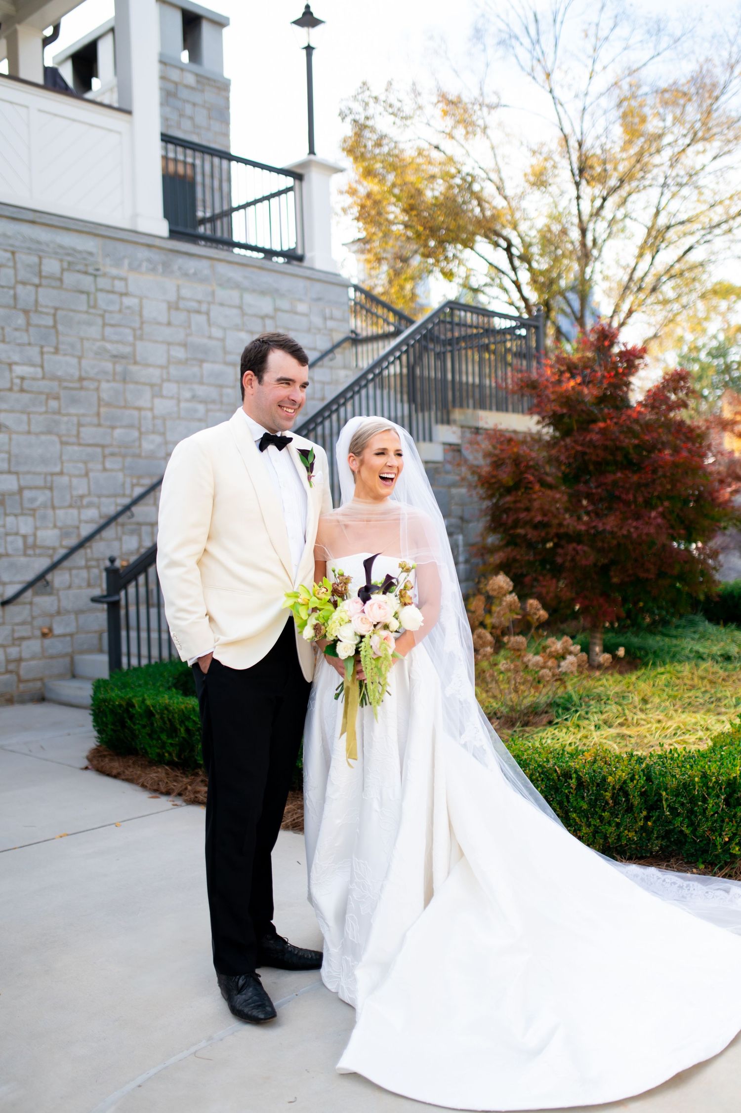 Outdoor wedding photos against stone architecture with autumn foliage in the background.