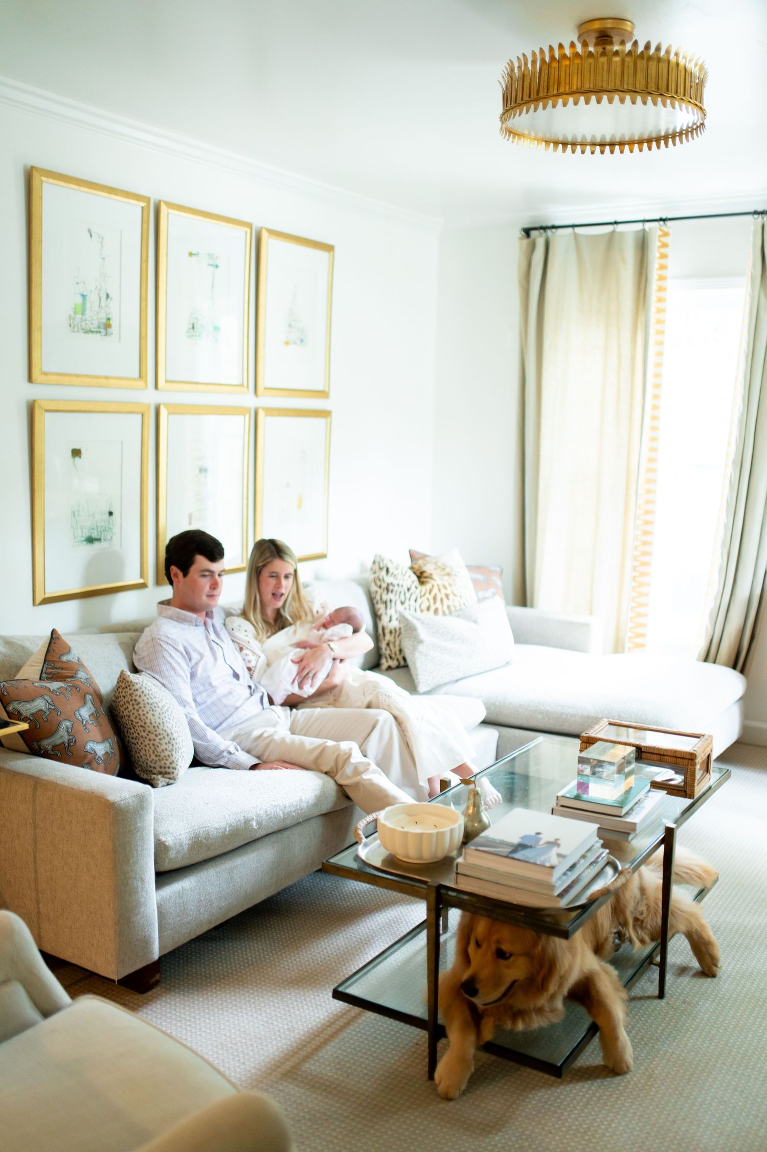 Bright living room interior with people relaxing on a gray sofa under a gold pendant light and framed artwork.