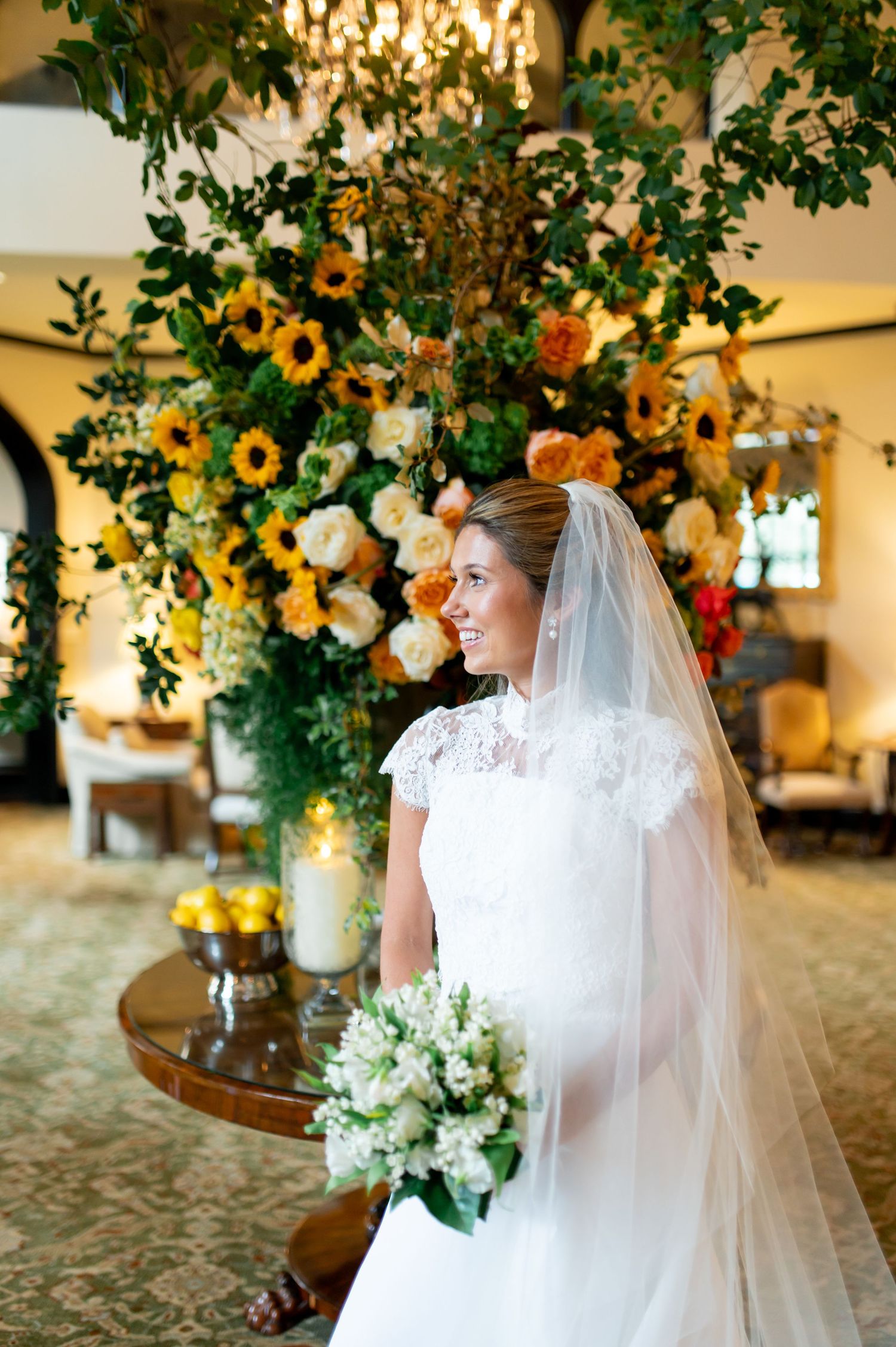 A bride in white dress poses near sunflower decorations in an elegant indoor setting.