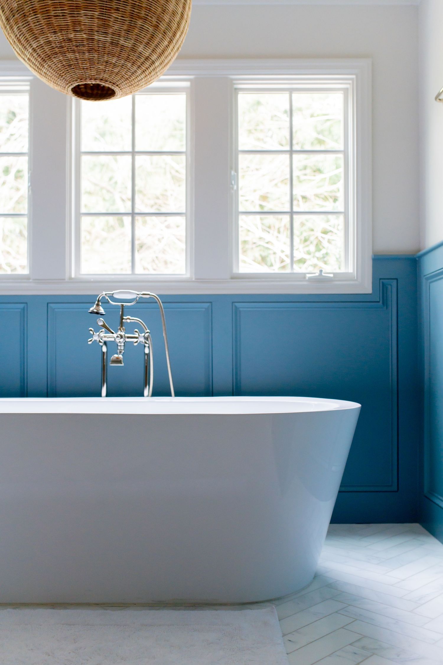 Minimalist bathroom featuring a freestanding tub, woven pendant light, and teal wainscoting beneath white walls.