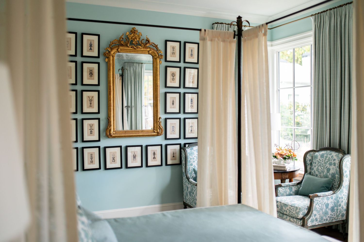 Elegant living room with teal walls, framed artwork gallery, ornate gold mirror, and white trim molding.