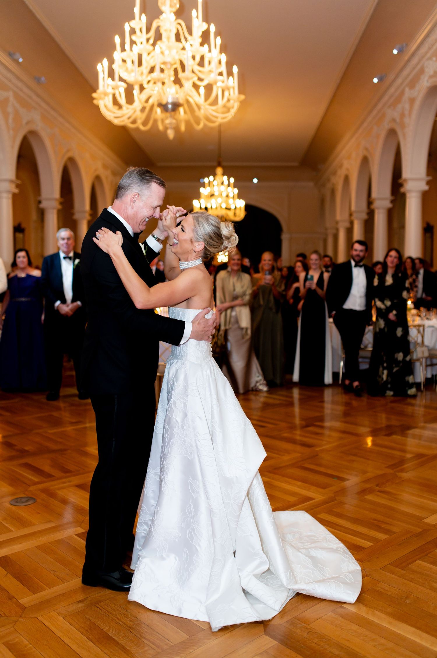 Newlyweds perform a dramatic dip during their ballroom dance under ornate chandeliers.