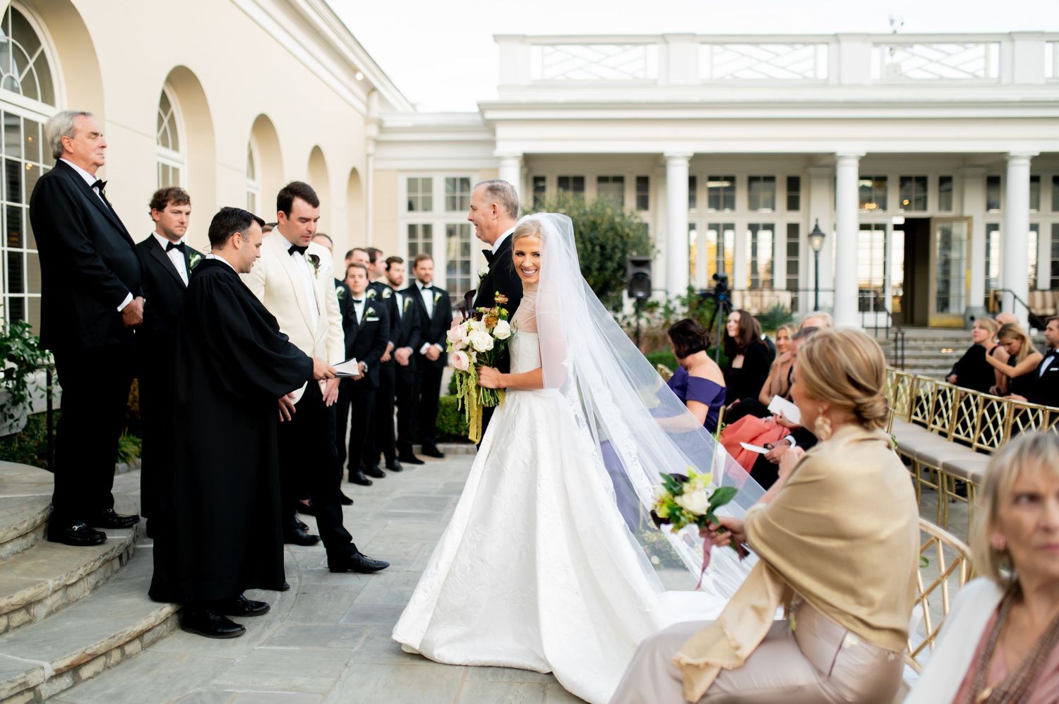 Wedding party processes across an elegant stone courtyard during formal ceremony.