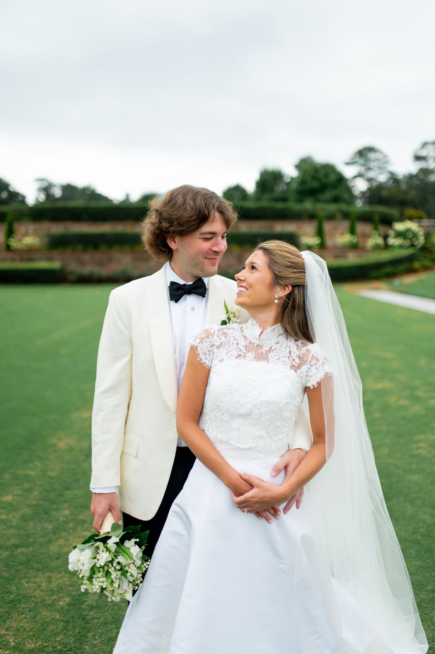 Romantic wedding portrait on green lawn with couple in white sharing a joyful moment.