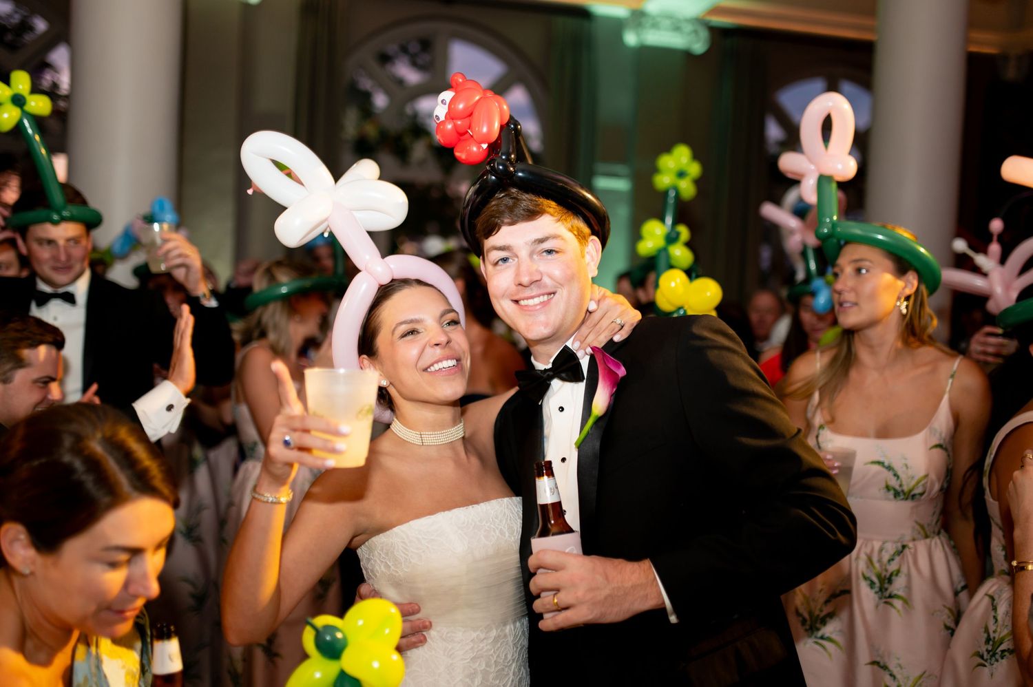 Bride and groom celebrate at wedding reception wearing fun balloon hats on the dance floor.