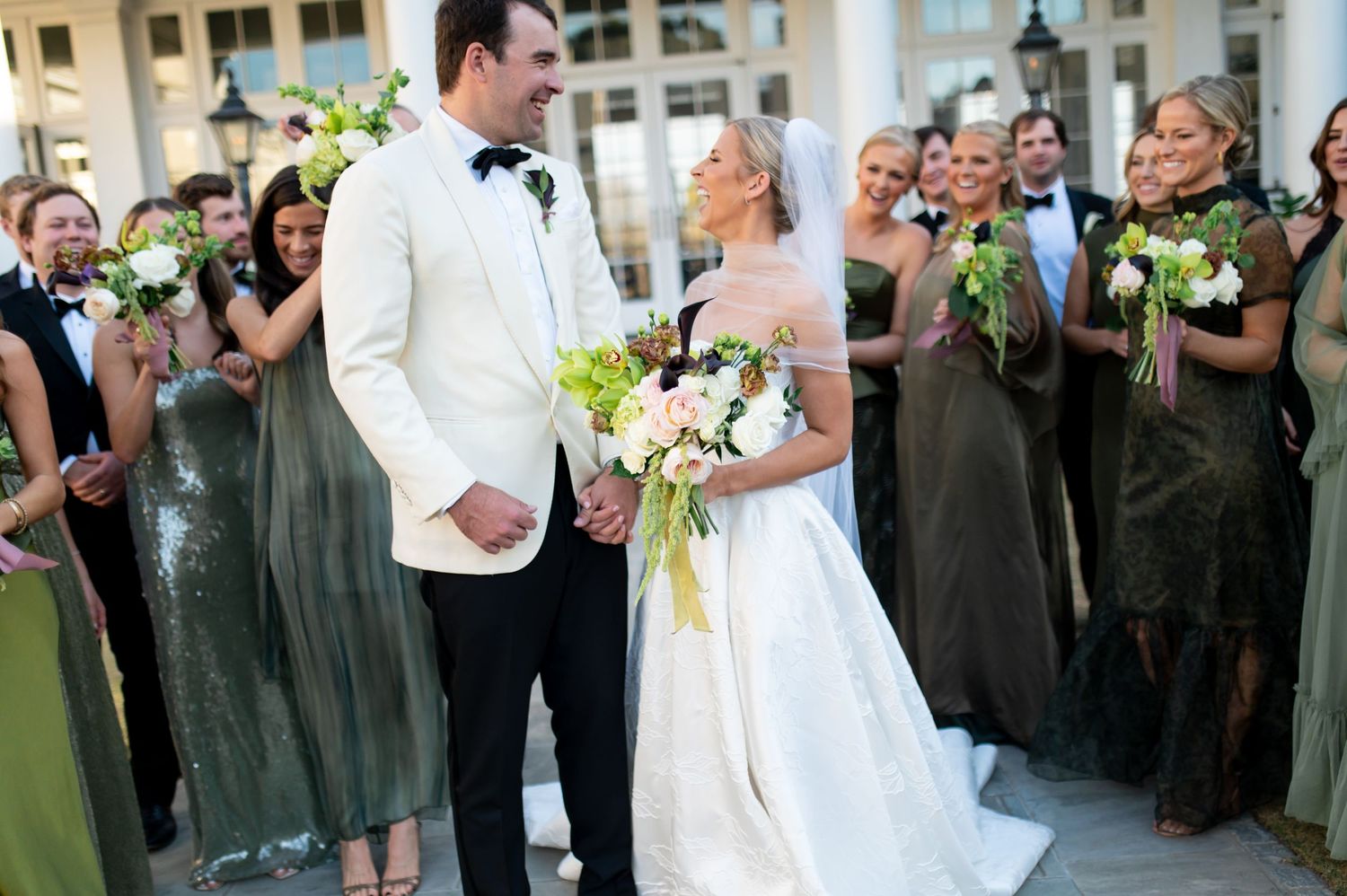 Wedding party gathers on an elegant white columned porch for formal photos.