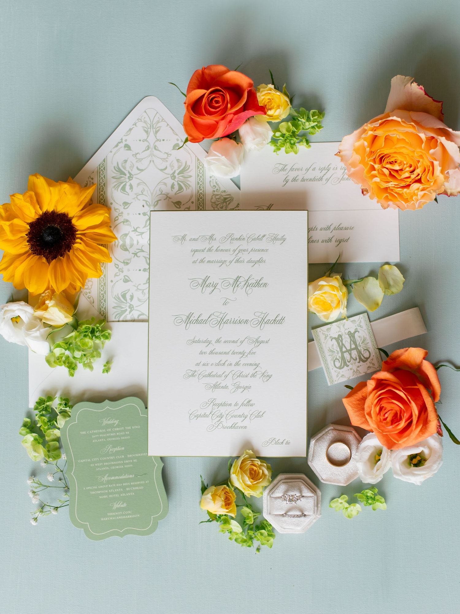 Wedding invitation suite with orange roses and sunflowers on light blue background.