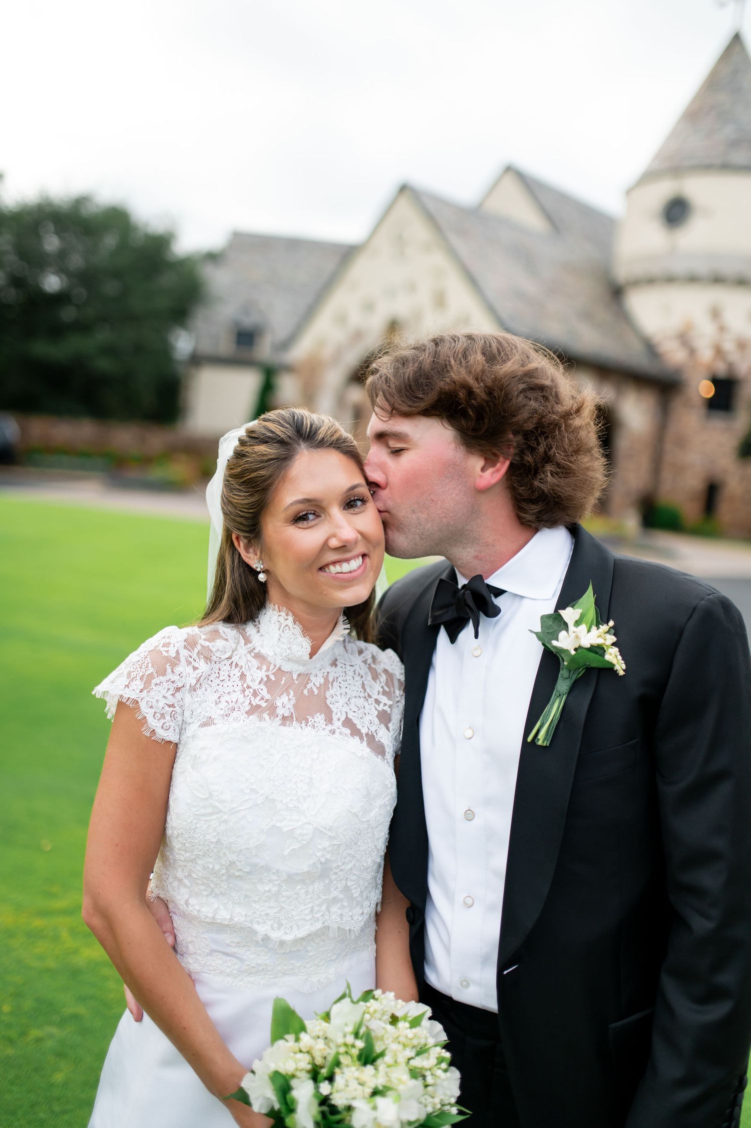 Romantic wedding portrait of couple with stone church and green lawn in background.