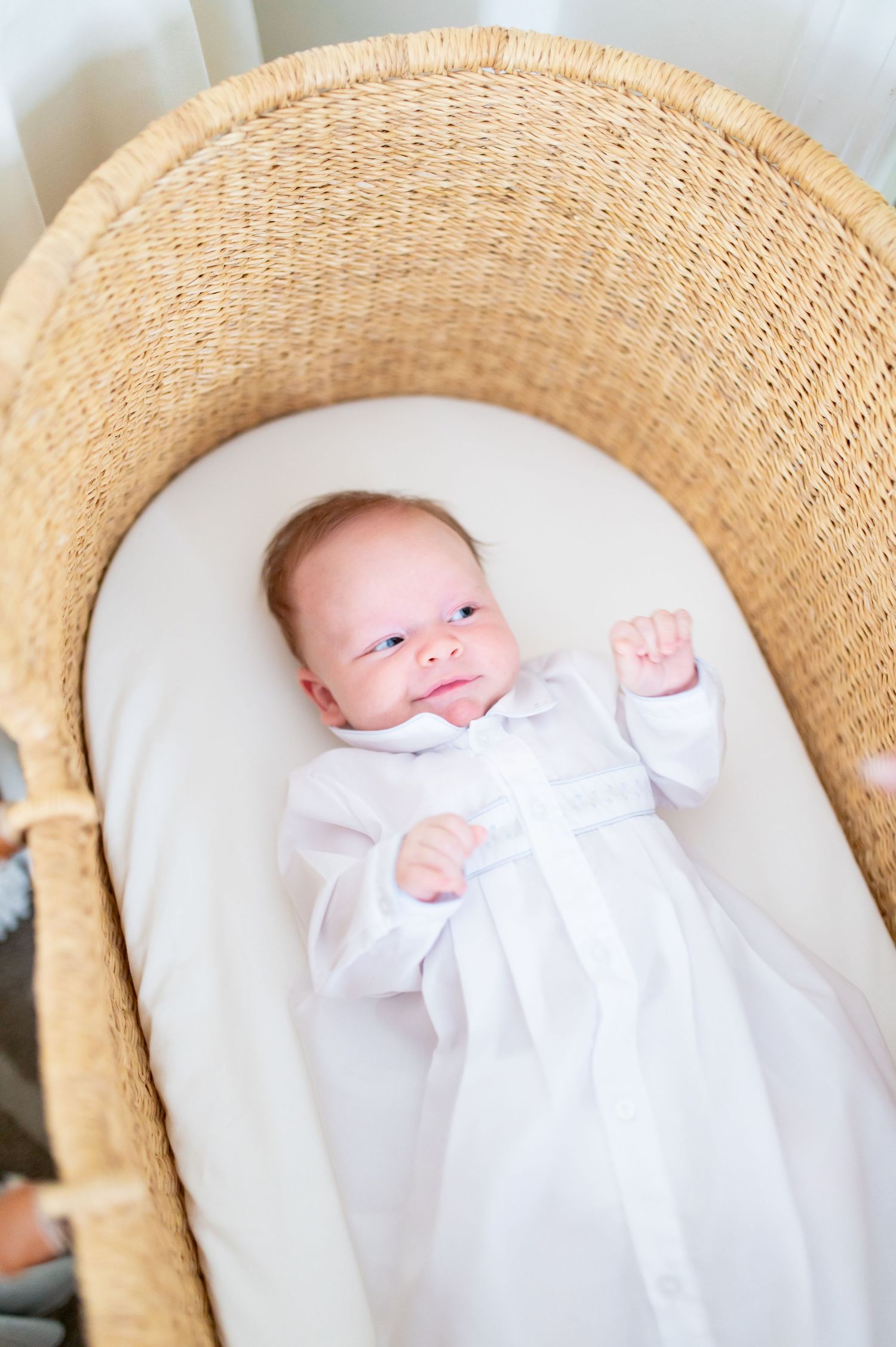 Newborn baby in white christening gown lying in a wicker Moses basket bassinet.