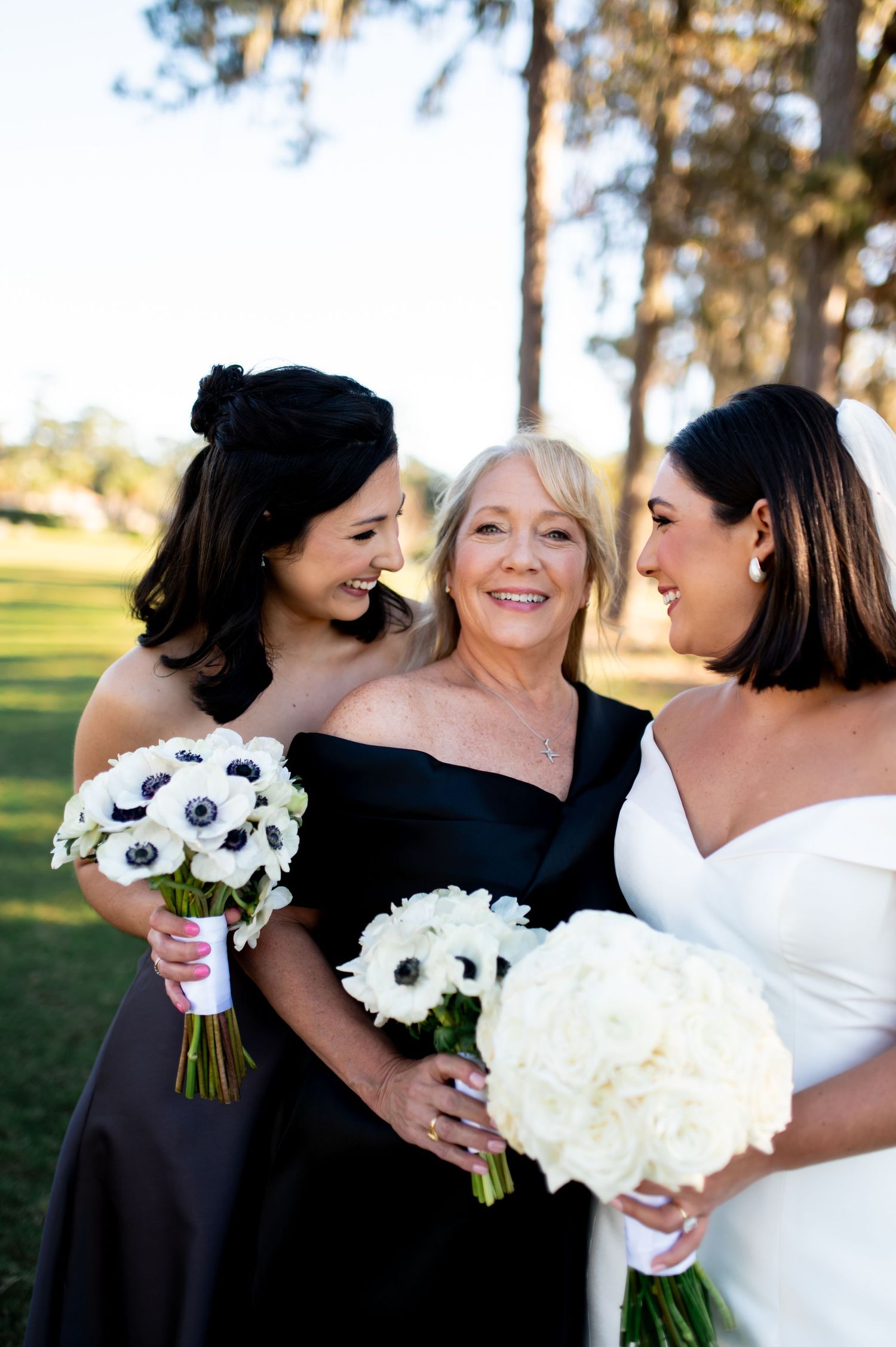 Wedding party members share intimate moments while holding white and black anemone bouquets.
